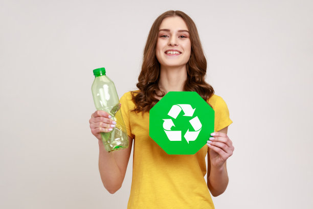 快乐满足的少女，棕色头发，黄色t恤，手里拿着回收牌子和塑料瓶，垃圾分类。图片下载