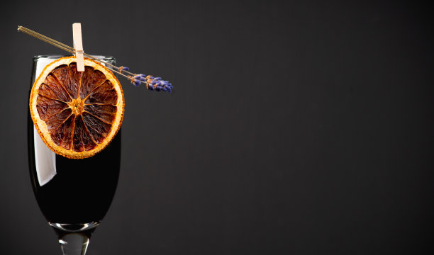 以香槟为主的黑色鸡尾酒，饰以薰衣草花和干橙。有选择性的重点。浅景深。图片下载