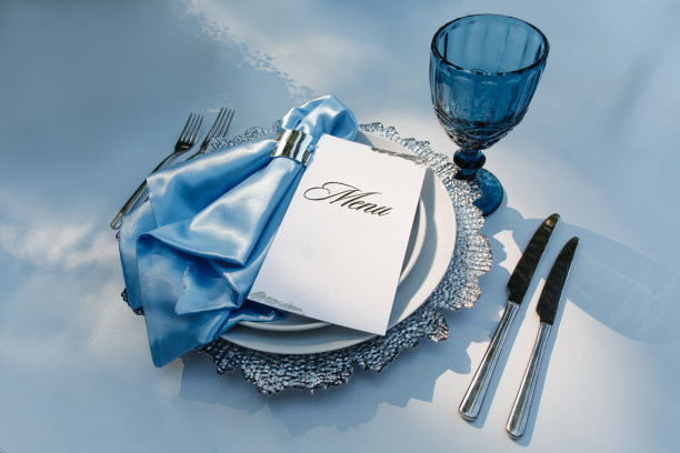 桌上的盘子上有刀叉和鲜花。优雅的桌子设置在蓝色柔和。图片下载
