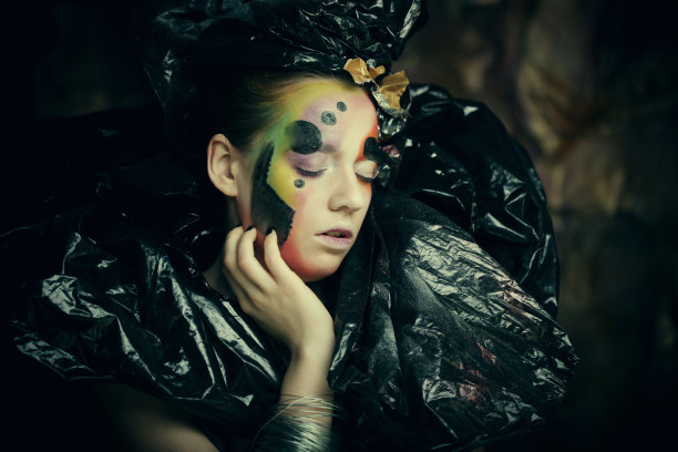 美丽的年轻女子与明亮的幻想化妆和服装在黑色的背景烟雾。万圣节图片下载