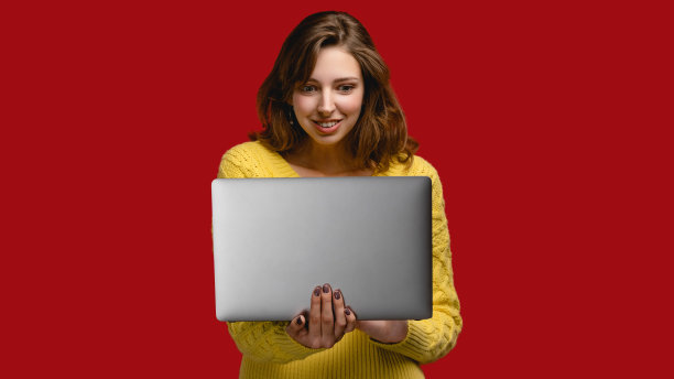 红色背景下，工作室里穿着黄色套衫的年轻女子。手提电脑概念图图片下载