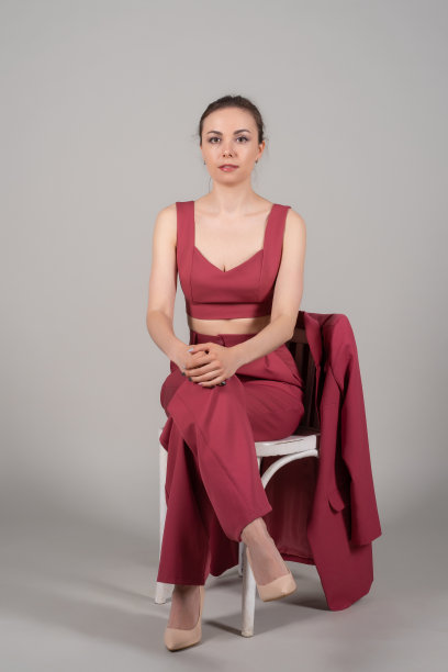 全身照片吸引别致的商务女士坐在椅子上，穿着红色西装，高跟鞋孤立的灰色背景图片下载