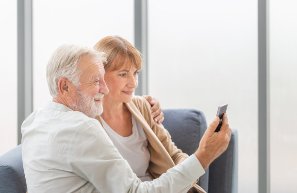 幸福的老夫妇在客厅的肖像，老女人和男人在舒适的沙发上用智能手机进行视频通话，幸福的家庭概念图片下载