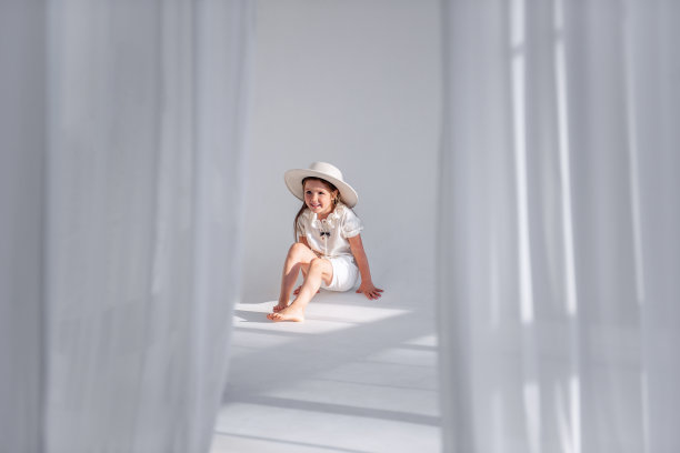 小女孩在地板上玩的很开心，戴着时髦的帽子，在一个白色的阁楼内部和通风的织物。图片下载