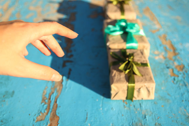 女手点上三个包裹的古董礼盒与橄榄色丝带蝴蝶结在蓝色(绿松石)古老的木制背景。礼品盒，创意图片。节日的概念。难看的东西脏桌子图片下载