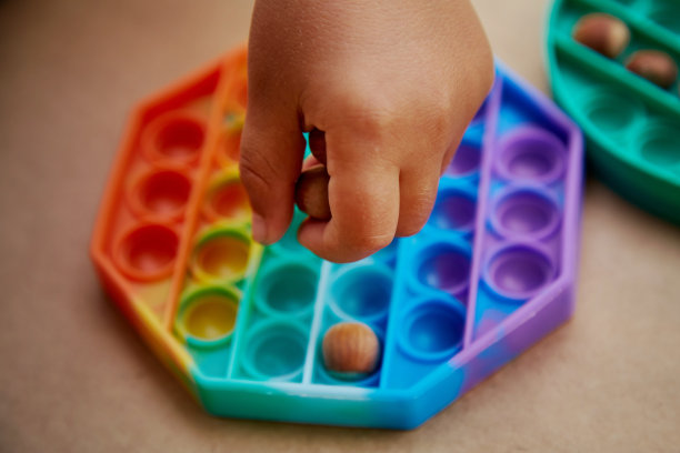 宝宝玩着pop it玩具和hazel。游戏为运动技能的发展。彩虹触摸感官的烦躁。前视图。高质量的照片图片下载