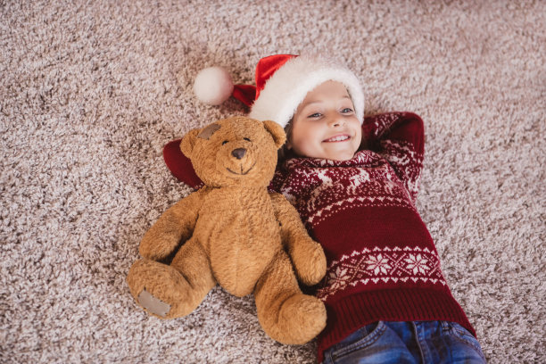 照片中，漂亮迷人的女学生穿着红色毛衣，头戴头巾，躺在地板上，胳膊在脑后，微笑着，在室内房间，家房子图片下载