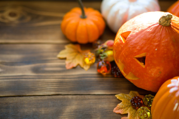 橙色和白色的南瓜和杰克灯笼，他的眼睛和嘴巴在木桌上与黄色的秋天枫叶，浆果。秋天心情，万圣节，家居装饰图片下载