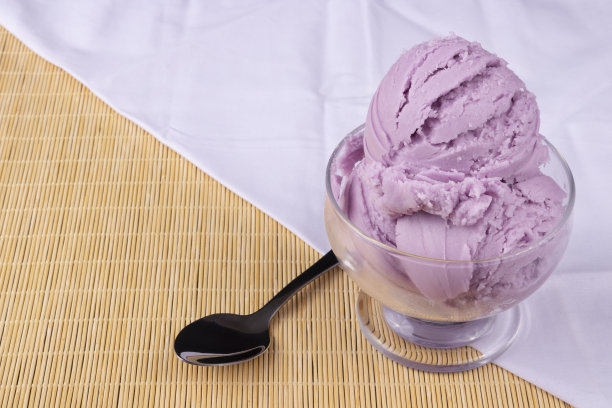 葡萄口味的紫色冰淇淋，盛在碗里，旁边有一个勺子。白色毛巾在底部对折。美食摄影冰淇淋店。图片下载