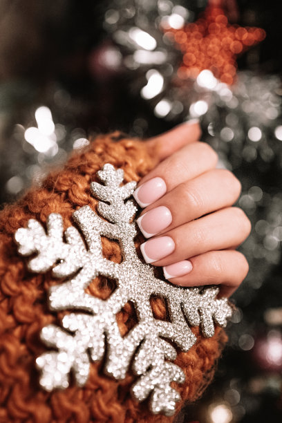 女手中拿着一片银白色的雪花，倚着圣诞树散景灯。新年寒假。图片下载