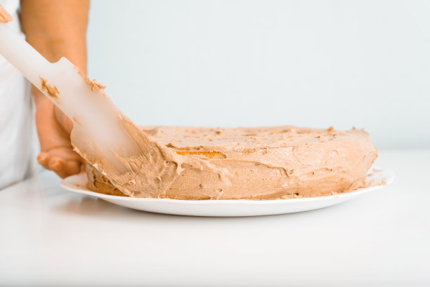 女厨师的手用抹刀装饰奶油馅蛋糕，主妇在白色的厨房桌子上准备分层美味的馅饼，特写。烹饪糖果图片下载