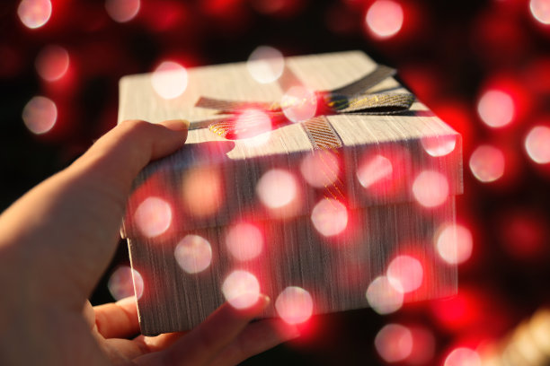 女性手握和给予包裹的复古礼盒丝带蝴蝶结在闪亮的暗红色散景背景。礼品盒，创意图片。节日的概念。闪闪发光的背景图片下载