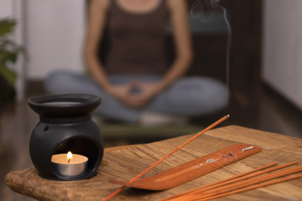 特写的香灯，木桌上的香，坐在垫子上练习瑜伽的女人图片下载