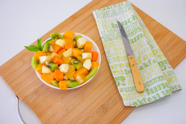 上图是一个白色的碗，里面装满了五颜六色的新鲜水果。苹果，猕猴桃，橘子，木瓜，芒果，甜瓜。早餐或休息，健康饮食图片下载