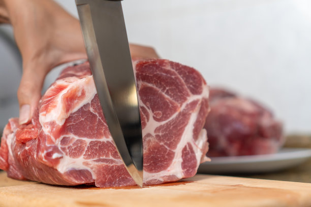 女人们的手用刀近距离切了一大块新鲜的猪肉放在砧板上，复制空间图片下载