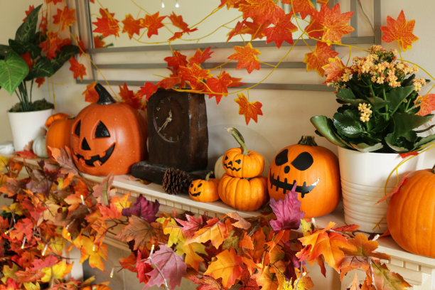 万圣节装饰展示的特写图像，橙色的葫芦与杰克O'灯笼风格的脸安排在木制时钟在壁炉架上与葫芦，秋天的彩色叶子，墙壁镜子和照明的弦灯图片下载