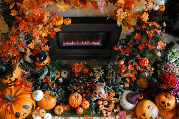 万圣节装饰展示的图像，巨大的橙色南瓜与杰克O'灯笼风格的脸排列在壁炉周围的葫芦，秋天的彩色叶子和照明的灯，高架的看法图片下载