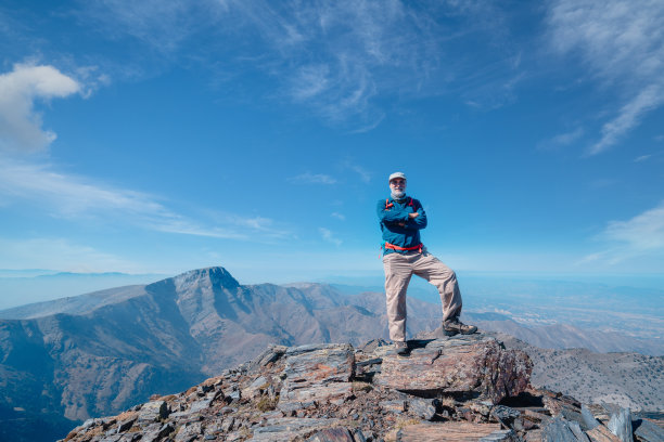 成功的年长登山者双臂交叉站在山顶图片下载