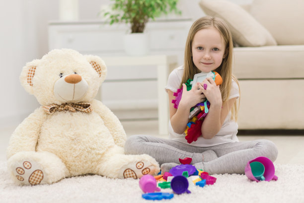 照片中的金发女孩拿着五颜六色的玩具看着相机。图片下载