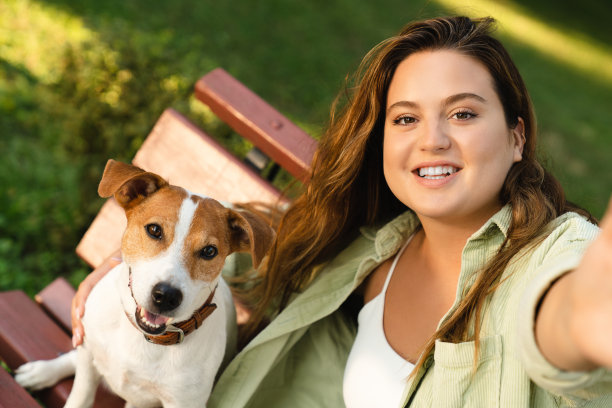 年轻的白人女学生自由职业者宠物主人与她可爱的杰克罗素梗自拍的正面照片，用于社交媒体，在公园户外发布视频通话。图片下载