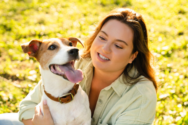 杰克罗素梗与年轻的宠物女主人在公园的绿色草坪上散步的近距离照片。狗的照顾收养概念。图片下载