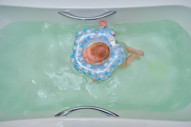 婴儿游泳，一个男孩在家里的浴缸里游泳，脖子上戴着一个充气环图片下载