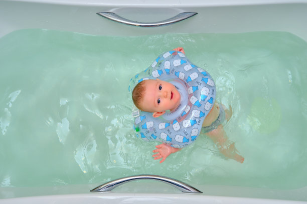 婴儿游泳，快乐男孩脖子上戴着充气环在家庭浴缸里游泳图片下载