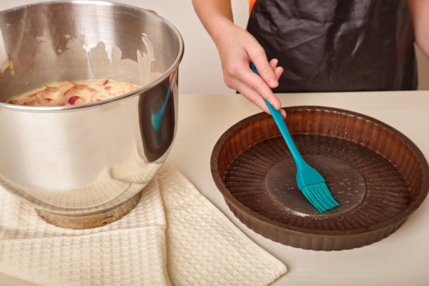 手用刷子润滑烤盘、烤盘。自制蛋糕的过程。一个穿着围裙的女孩在家里的厨房里准备自制的蛋糕、纸杯蛋糕、馅饼图片下载