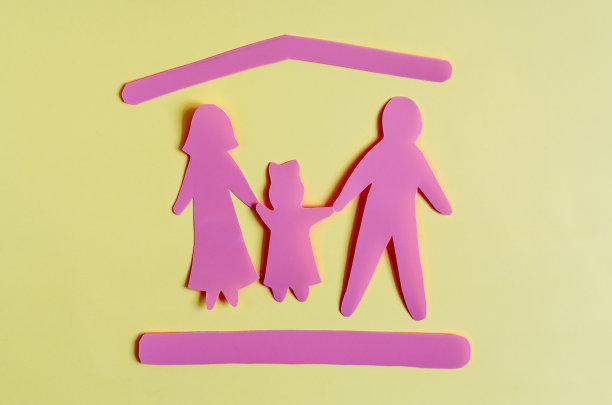 两个大人和一个小孩的纸板人物在红色的屋顶下，象征着保护，在彩色的背景上。家庭的社会保护和保险保护的概念。图片下载