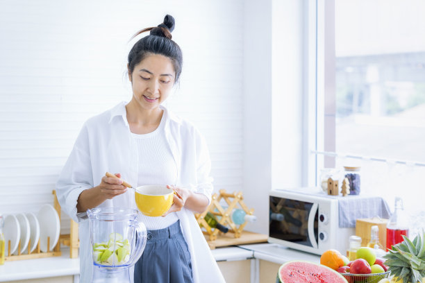 亚洲女人在厨房里做果汁和冰沙。女人在厨房用搅拌器做冰沙图片下载