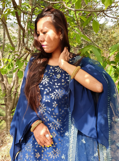 一个美丽的亚洲年轻女孩穿着蓝色的裙子和触摸她的头发向下看，人们在自然中摆姿势-股票照片图片下载