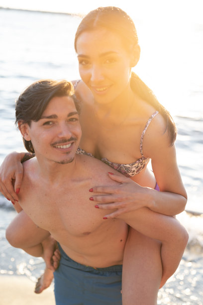 照片上是一对年轻美丽的情侣，男孩和女孩，在海滩上约会，她骑在他的肩膀上——一对男女恋人在阳光明媚的日子里站在海边图片下载