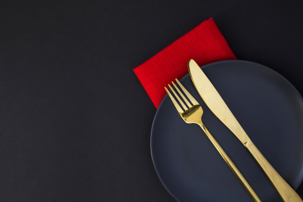 节日餐桌，黑色背景上黑色盘子上的金色刀叉。前视图。副本的空间。图片下载