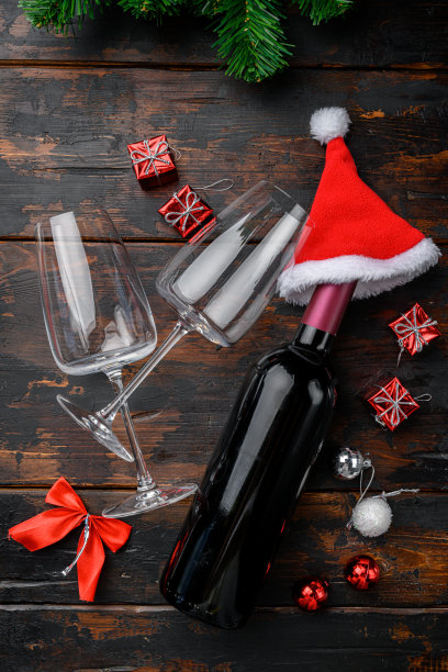 圣诞老人戴着红帽子的酒瓶，放在旧的深色木桌背景上，俯视图平放图片下载