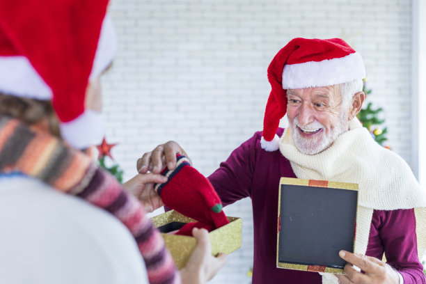 白种人老爷爷带着红色的圣诞老人帽，在家中兴高采烈地打开家人送给他的圣诞礼物图片下载