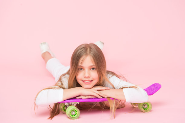 滑板创造了潮人。可爱的小溜冰者微笑着嬉皮士的风格和外观。可爱的小潮人在粉红色背景的滑板上放松。快乐的嬉皮士与紫罗兰便士板图片下载