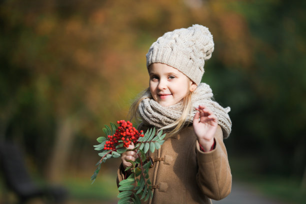 可爱的小女孩手里拿着一根花梨树的树枝，手里拿着红色的浆果，挥手问好。图片下载