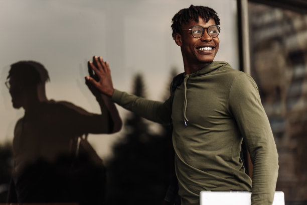 一个美国商人，背着背包，拿着笔记本电脑，戴着眼镜在大楼前摆姿势图片下载