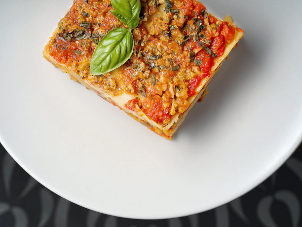 白色盘子上放一片罗勒叶的千层面。特写，俯视图。图片下载