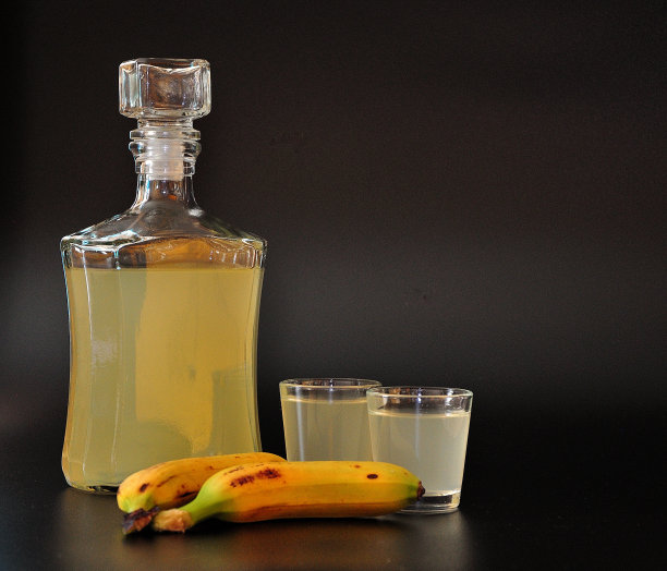 自制的香蕉利口酒，装在一个玻璃瓶里，两个玻璃杯，黑色背景。图片下载