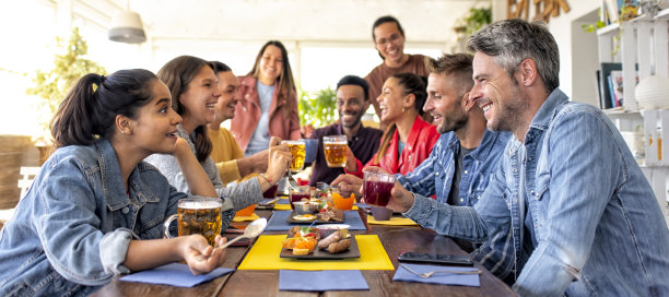 快乐的多元文化的一大群朋友一起在酒吧餐厅的咸早餐早午餐室内。爱交际的人们坐在家里的桌子上谈笑风生。生活方式的概念图片下载