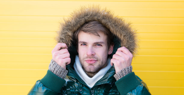 保暖。舒适的冬季服装。冬季时尚男装。留着大胡子的嬉皮士穿着暖和的皮草黄色背景夹克。男人穿暖和的夹克和兜帽。穿暖和的衣服感到舒适图片下载