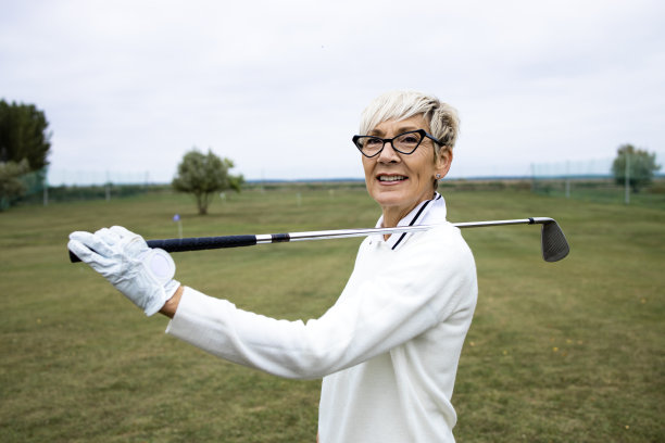 女高尔夫球手拿着高尔夫球杆站在高尔夫球场上的照片。图片下载