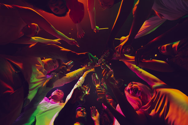 碰杯的底部视图。一群年轻，活跃的人在夜总会，在霓虹灯下聚会，喝着鸡尾酒图片下载