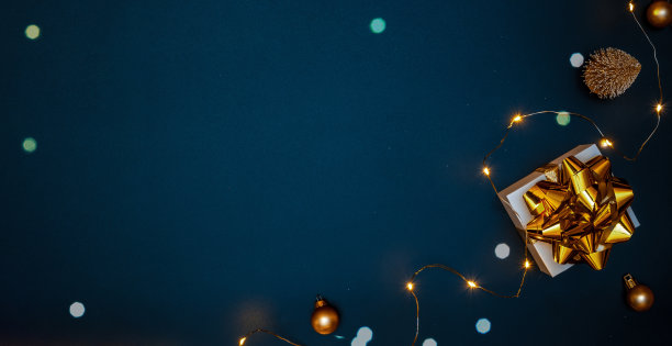 圣诞礼物。白色的礼物与金色的蝴蝶结，金球和闪闪发光的灯在圣诞节装饰在黑暗的背景贺卡。圣诞节背景与空间的文本。图片下载