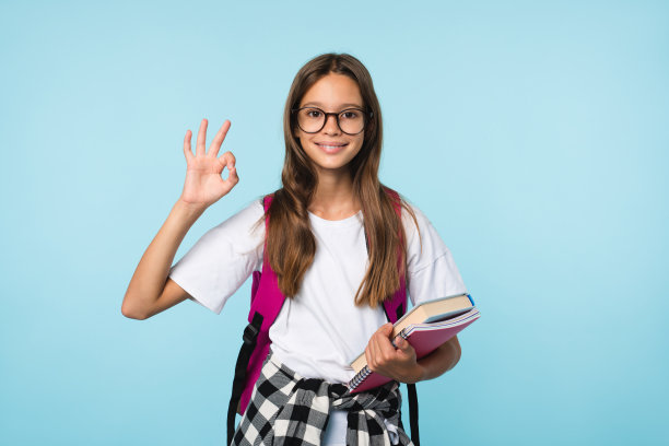 蓝色背景下露齿微笑的比OK手势的白人少女学生特写肖像图片下载