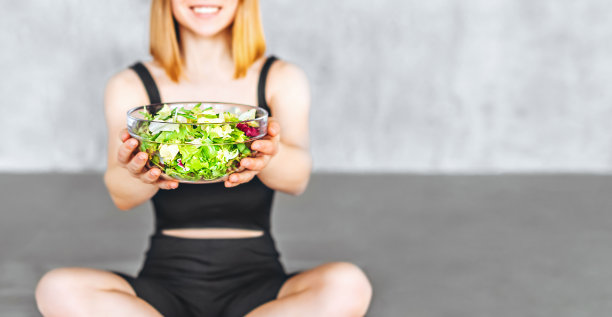 一个穿着运动服的运动女人正拿着健康食品坐在地板上。图片下载