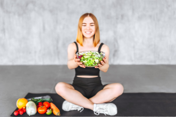 一个穿着运动服的运动女人正拿着健康食品坐在地板上。图片下载