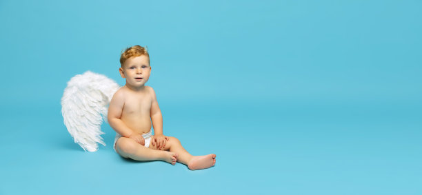 全身肖像小男孩，孩子在尿布与天使翅膀平静地坐在孤立的蓝色背景。摩天观景轮图片下载