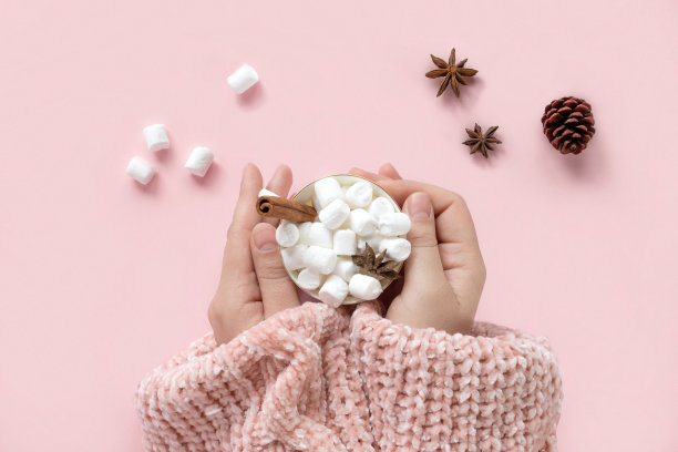 冬季饮料，白色杯子与棉花糖在女性手中针织圣诞毛衣粉红色的背景。俯视图，平放。新年、圣诞节的传统食品。节日装饰，庆祝圣诞节图片下载